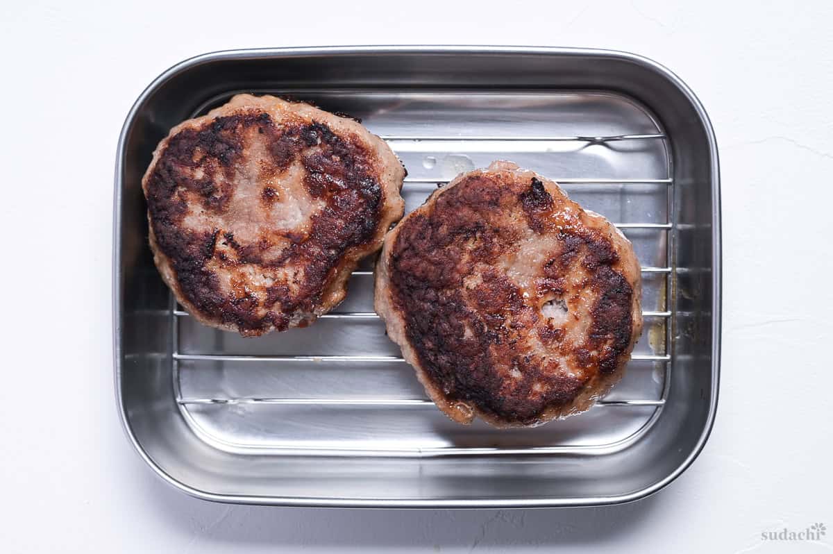 two cooked pork patties resting on a wire rack