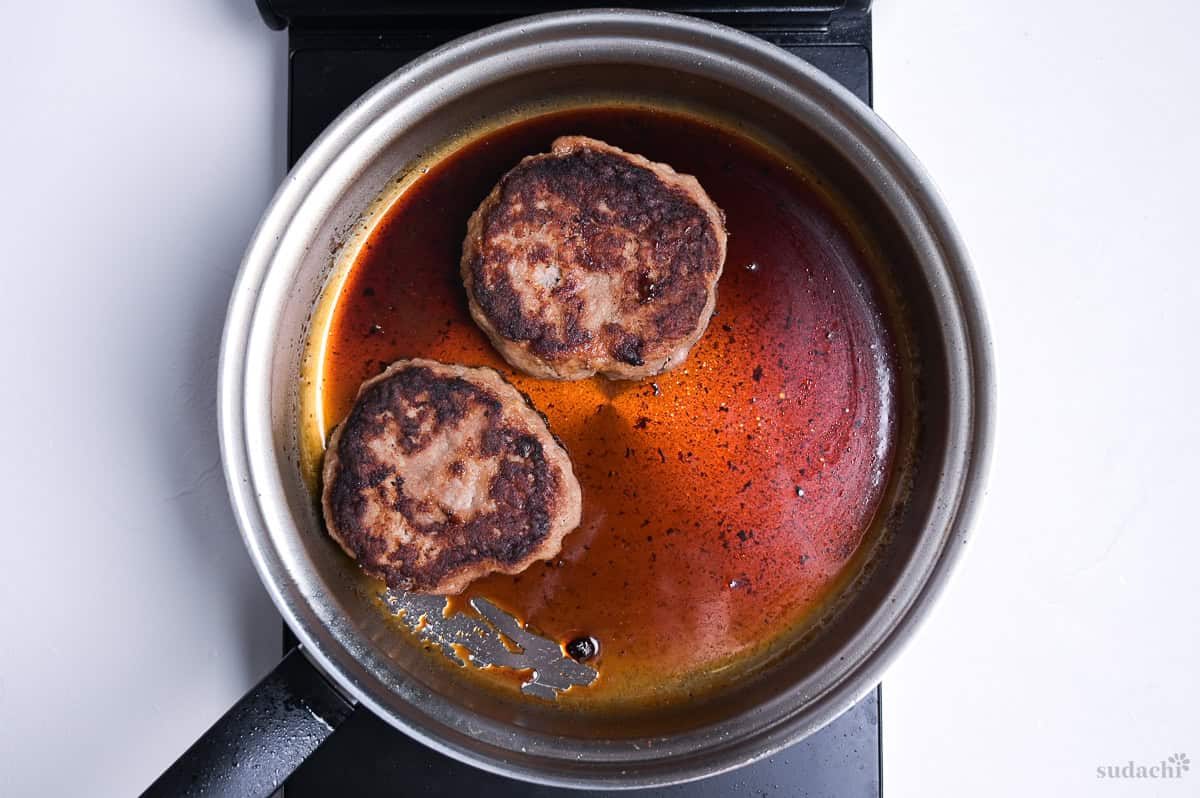 two pork patties placed in a pan with teriyaki sauce