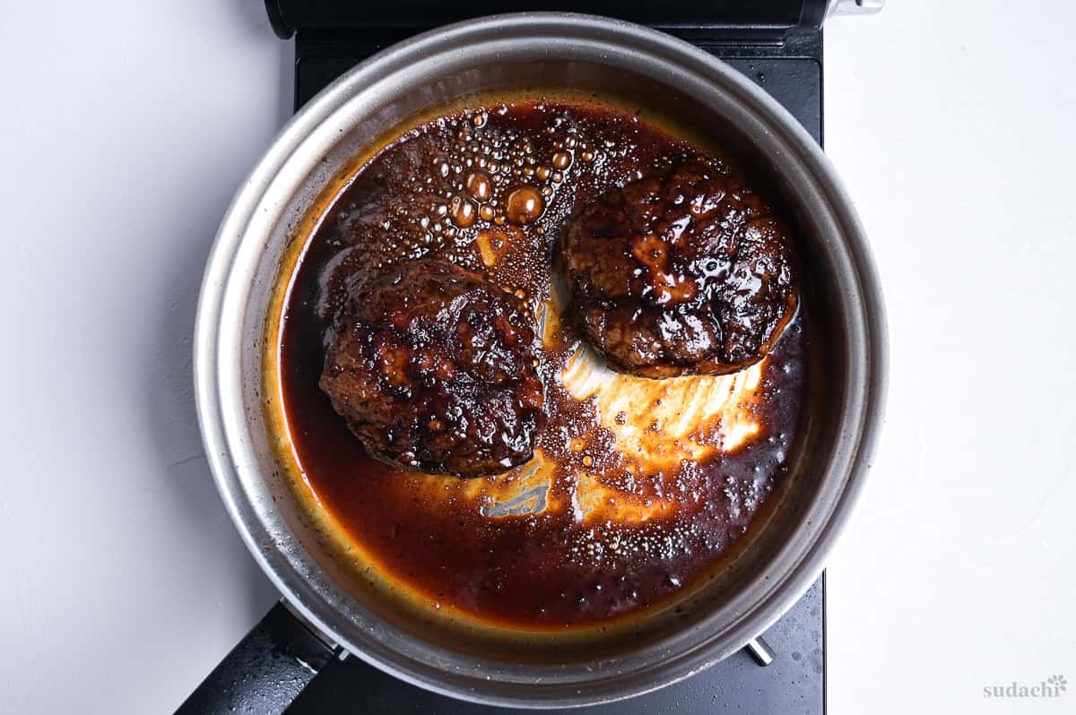 thickened teriyaki sauce coating two pork patties in a frying pan