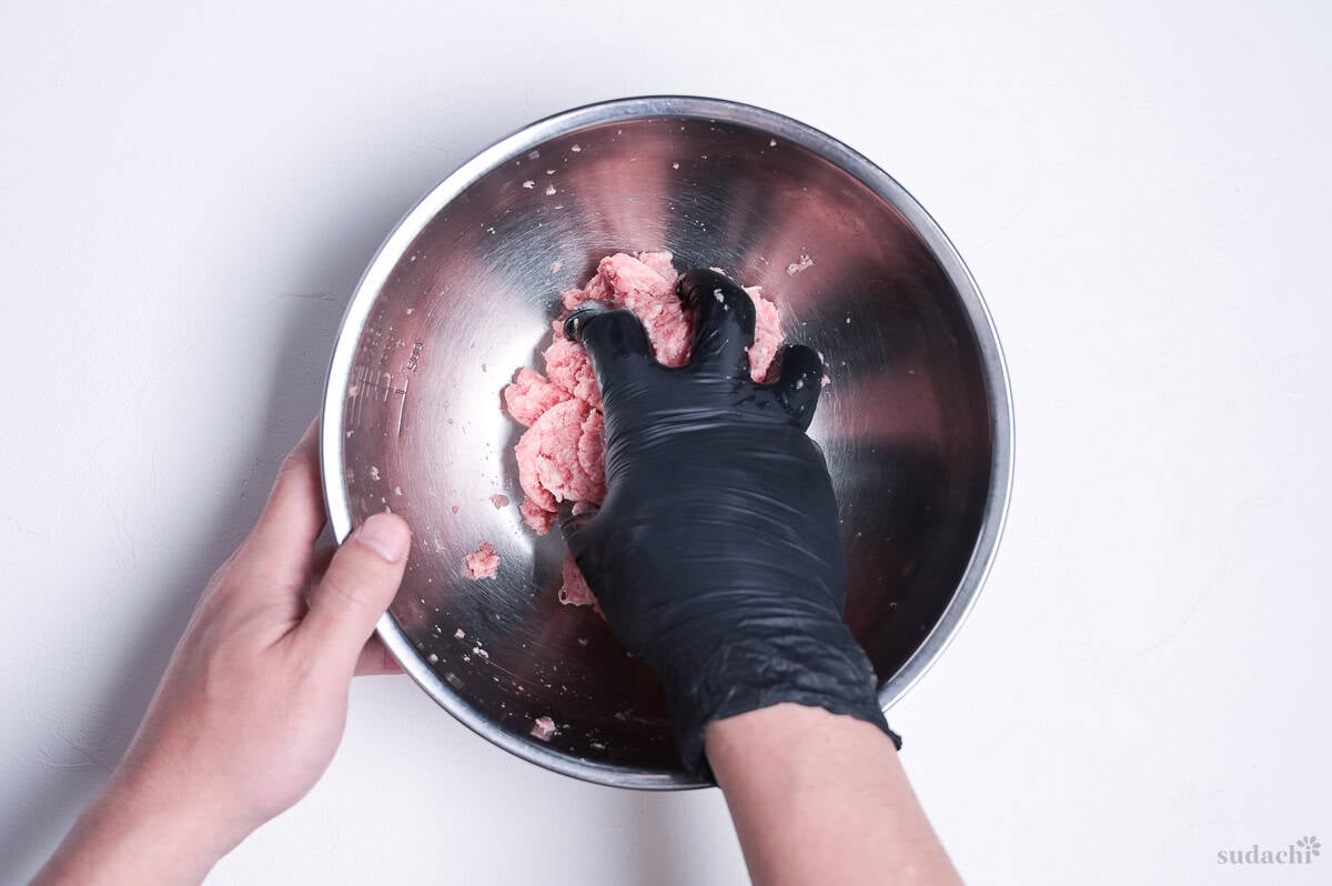 kneading ground pork in a large metal mixing bowl