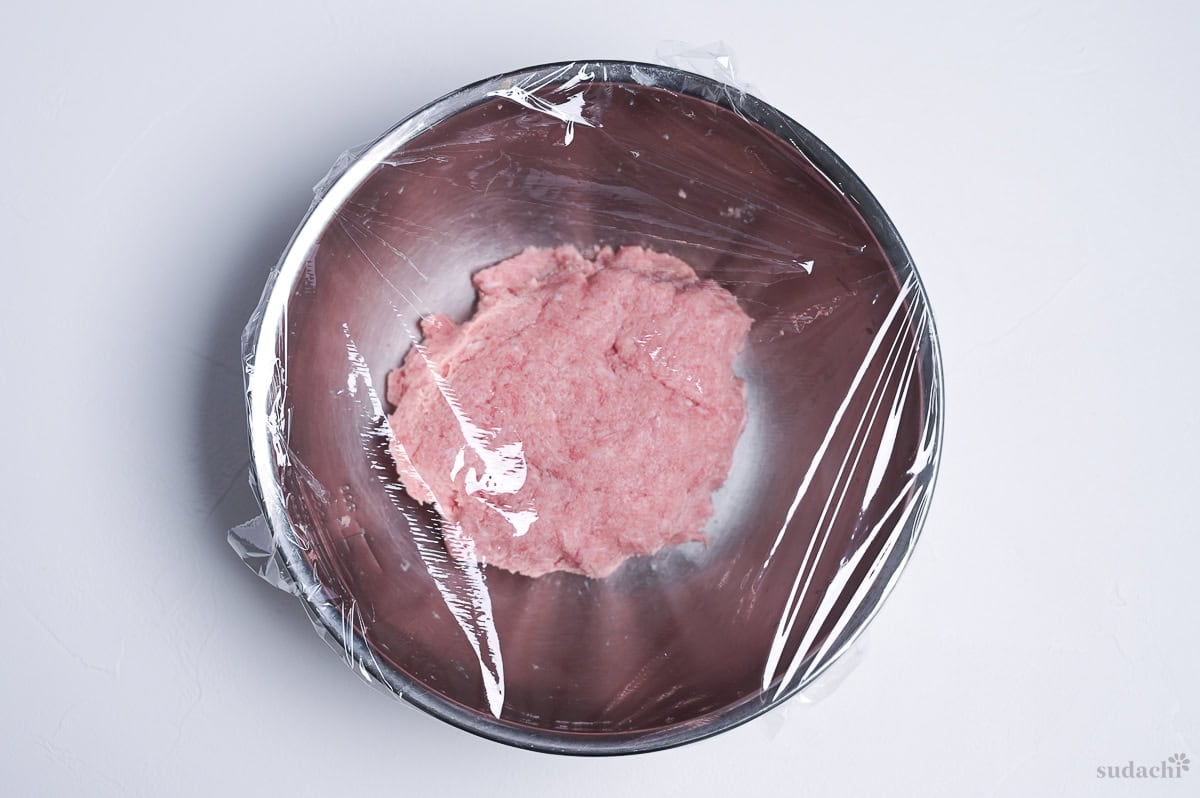 kneaded ground pork for teriyaki burger patties in a steel mixing bowl covered with plastic wrap