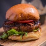 Teriyaki burger with lettuce, tomato and pickled ginger on a wooden cutting board