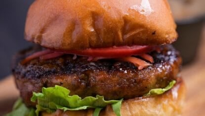 Teriyaki burger with lettuce, tomato and pickled ginger on a wooden cutting board