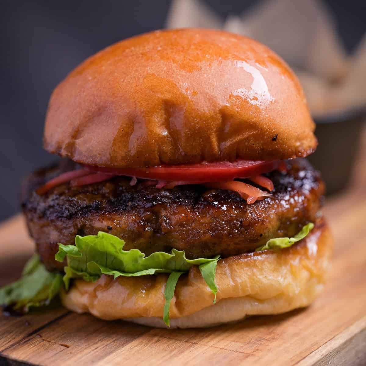 Teriyaki burger with lettuce, tomato and pickled ginger on a wooden cutting board
