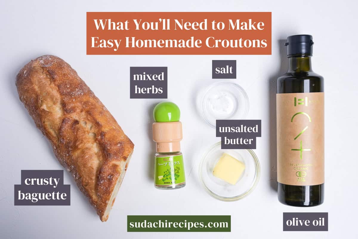 Ingredients needed to make homemade croutons with baguette on a white background with labels. From top to bottom, left to right: crusty baguette, mixed herbs, salt, unsalted butter, olive oil.