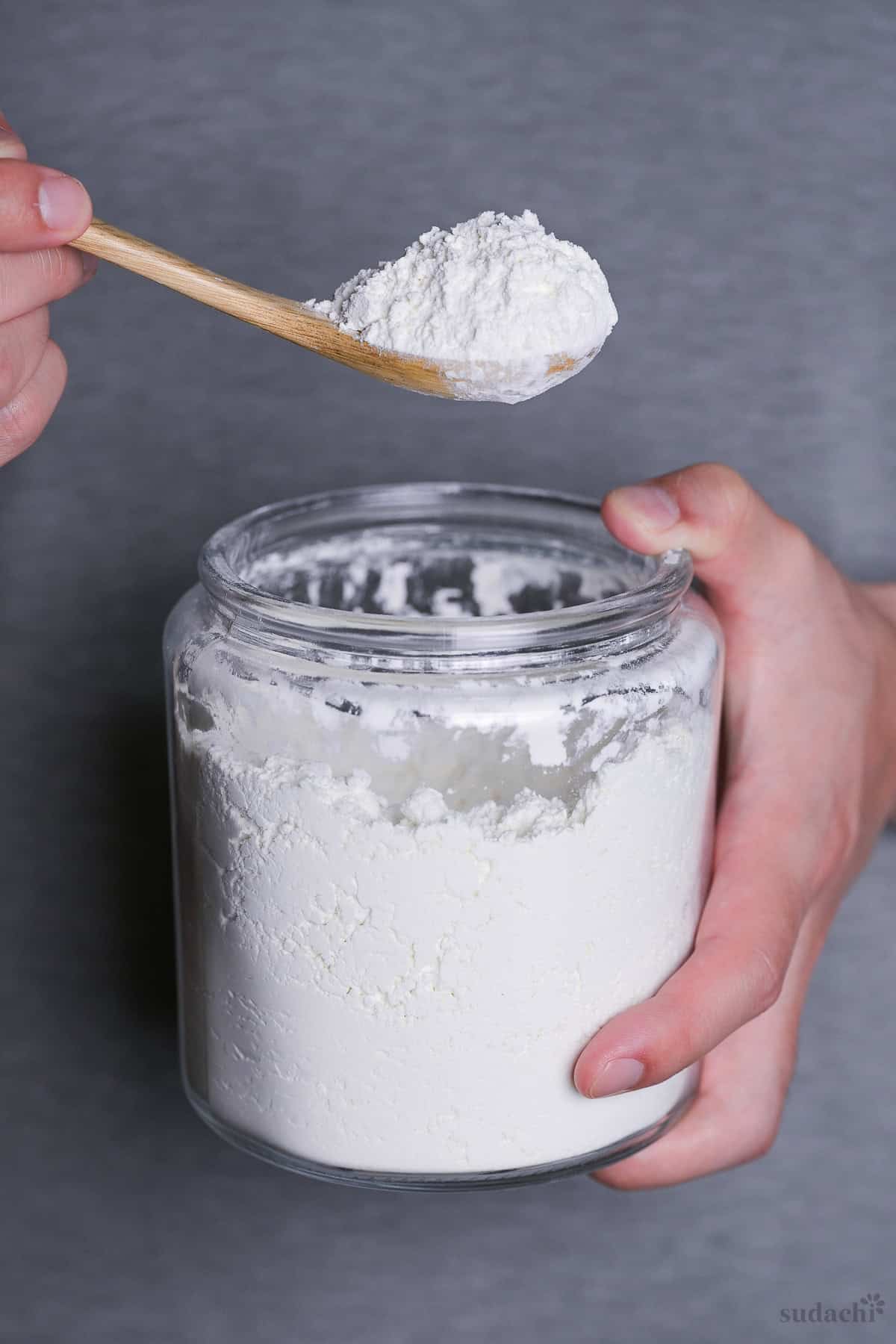 Yuto Omura holding a glass jar of flour with a scoop of flour on a wooden spoon