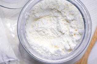 Low protein flour in a glass jar next to bagged flour and a wooden spoon for thumbnail