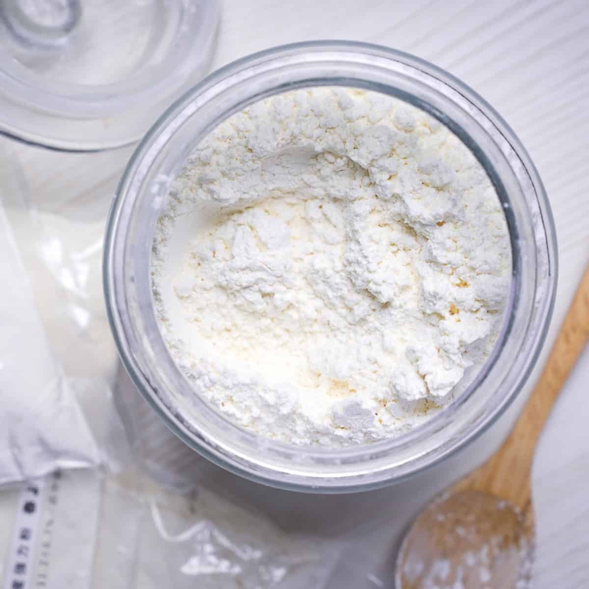 Low protein flour in a glass jar next to bagged flour and a wooden spoon for thumbnail