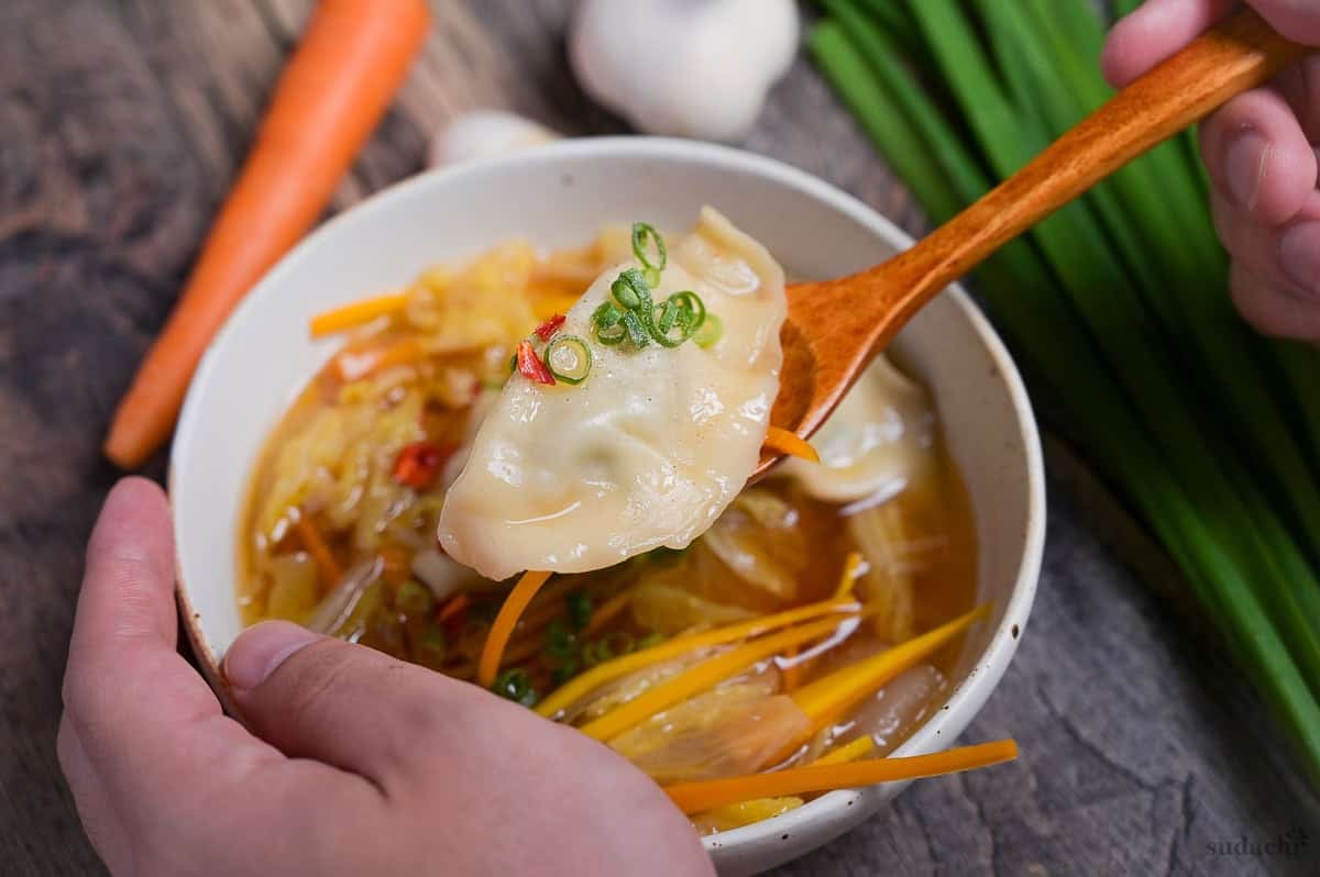 Homemade gyoza soup with a wooden spoon holding up one gyoza topped with some chopped green onion and chili