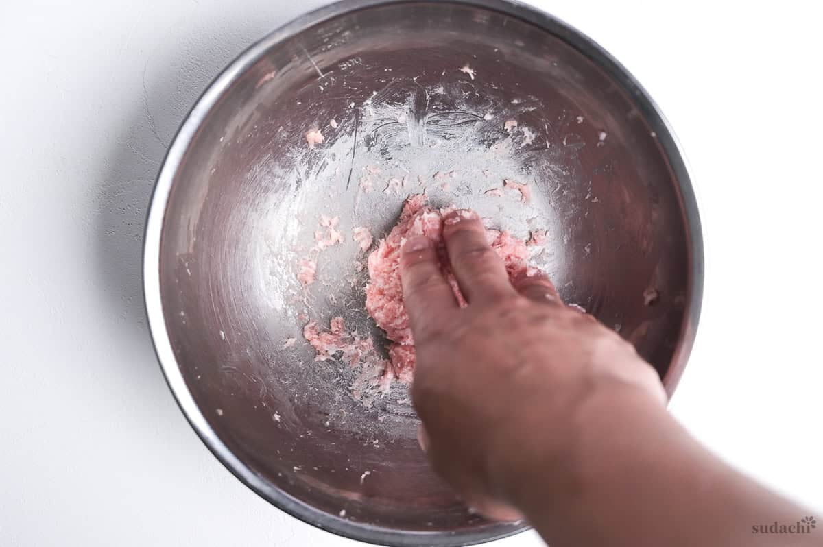 Kneading ground pork with salt in a steel mixing bowl