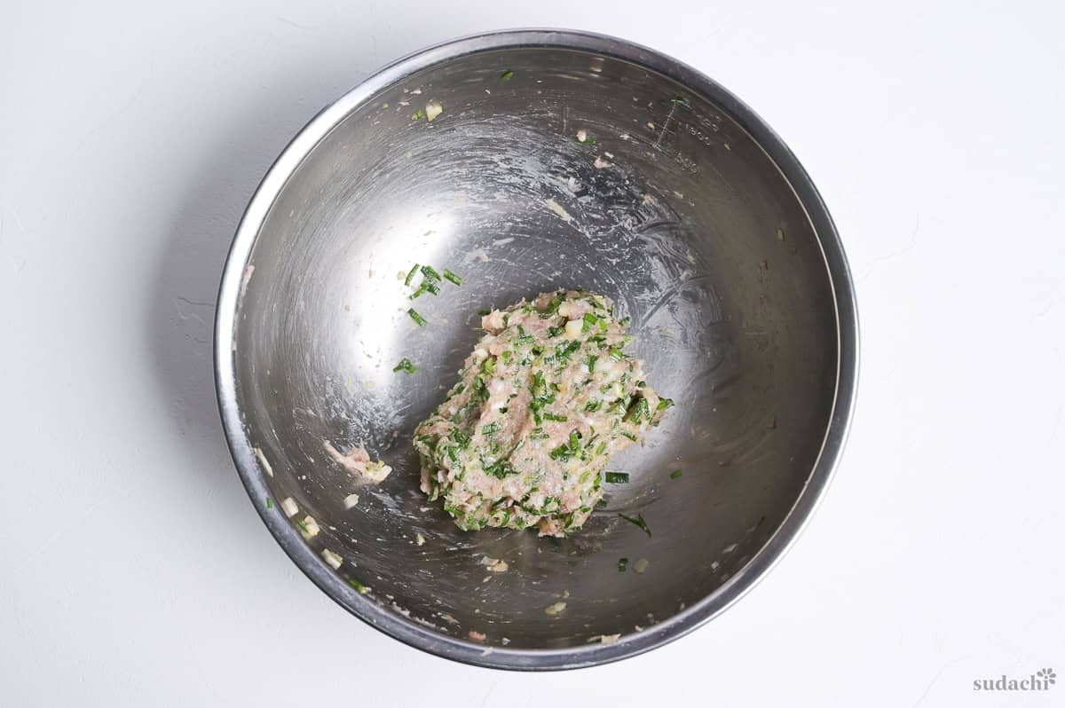 Gyoza soup gyoza filling made with pork, in a steel mixing bowl on a white background.