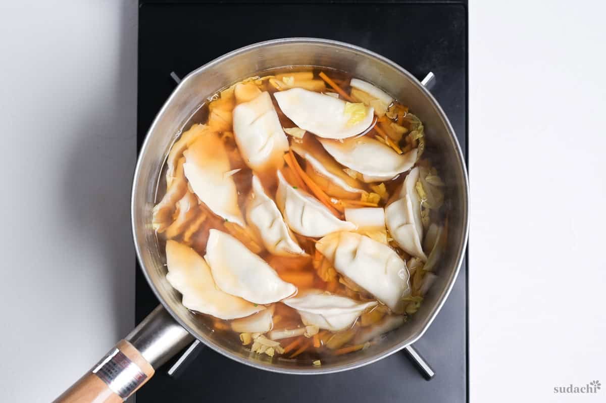 Gyoza simmering in soup in a pot on the stove top.
