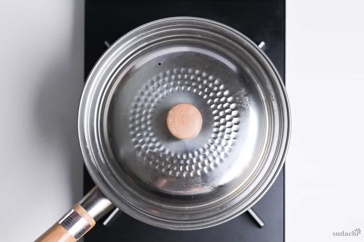 Gyoza soup cooking in a pot with a lid on, on the stove top