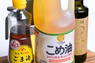 Various bottled oils on a wooden cutting board including toasted sesame oil, rice bran oil, and extra virign olive oil.