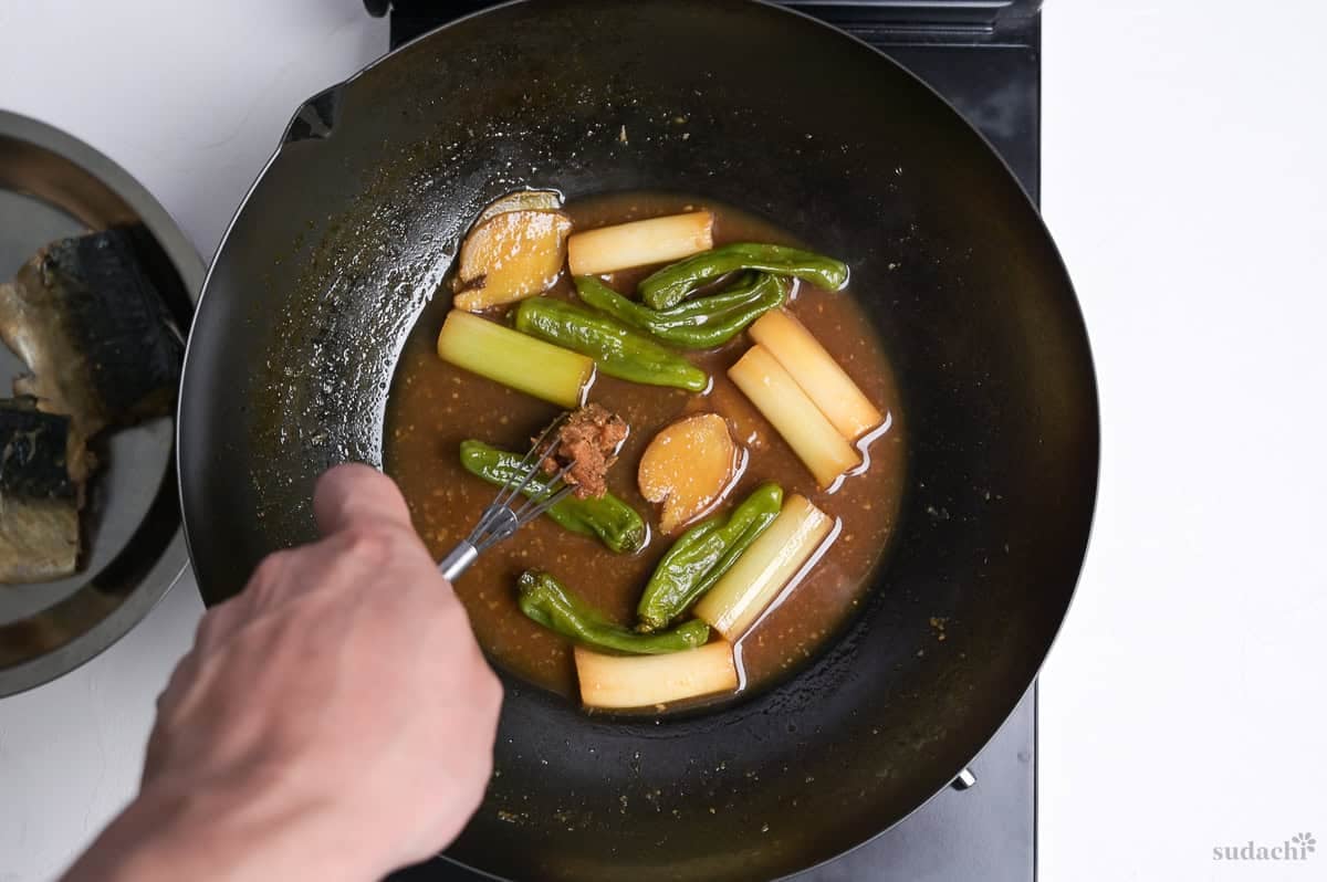 Adding miso to miso simmered mackerel broth in a pan.
