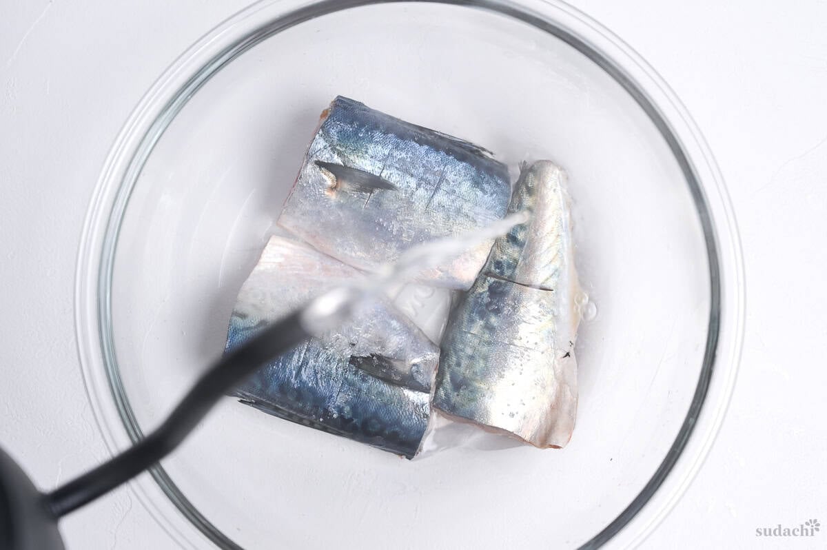 Three mackerel fillets in a glass bowl with boiling water being poured over them.