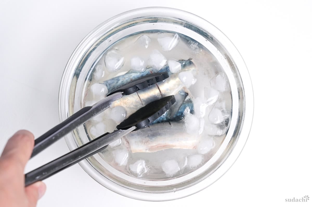 Three mackerel fillets in a glass bowl filled with ice water.