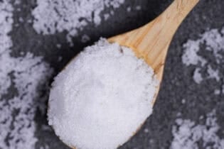 Japanese sea salt heaped on a wooden spoon on a mottled gray background.