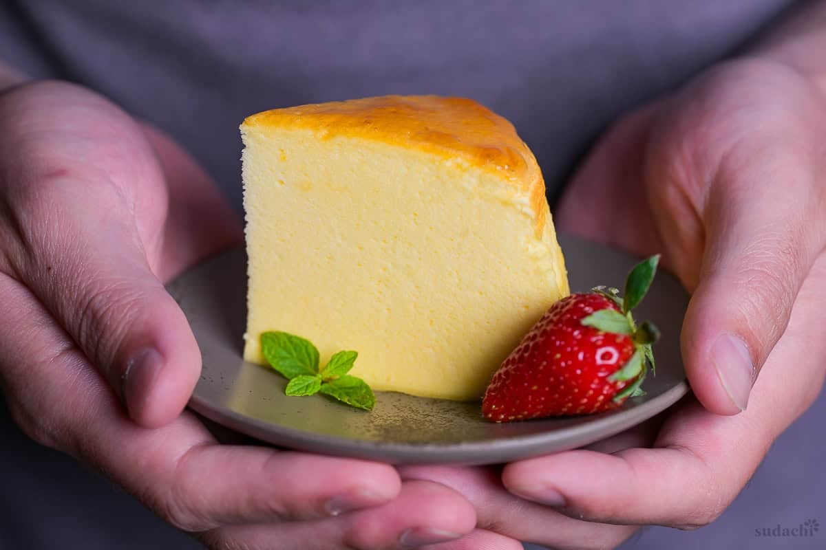Yuto Omura holding up a piece of Japanese soufflé cheesecake on a gray plate with a mint leaf and a strawberry