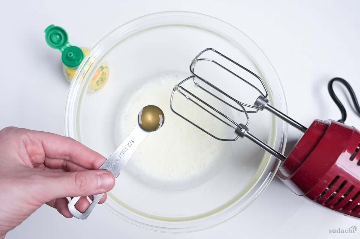 pouring lemon juice into whisked egg whites in a glass bowl