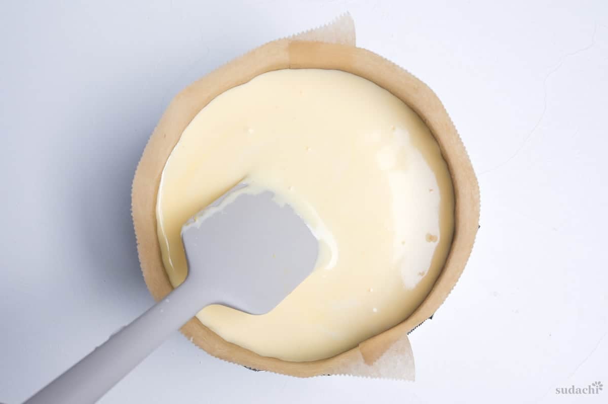 soufflé cheesecake batter in a lined cake pan with spatula