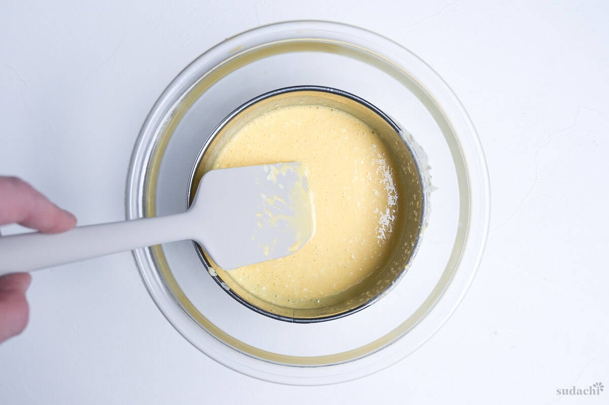 straining Japanese soufflé cheesecake mixture through mesh sieve into a glass bowl