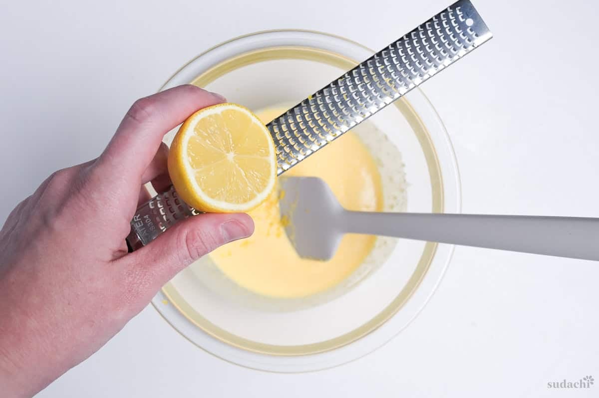 using a microplane grater to zest a lemon into soufflé cheesecake mixture