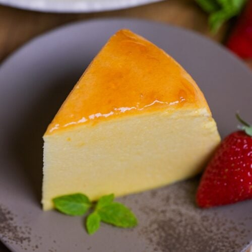 Japanese souffle cheesecake on a gray mottled plate with a mint leaf and a strawberry