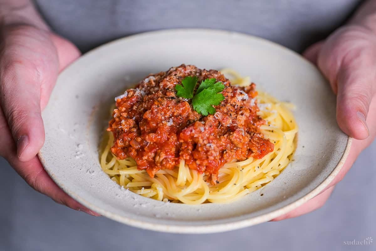 Yuto Omura holding Japanese style spaghetti meat sauce topped with grated cheese and a piece of fresh parsley in an off-white pasta dish
