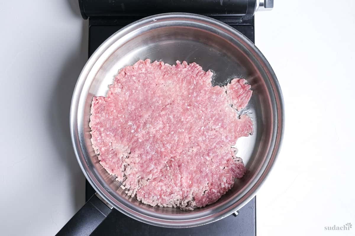 Ground pork pressed into a thin layer in a stainless steel pan on the stove top