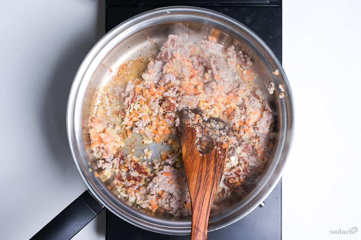 ground pork and finely diced vegetables in a stainless steel pan to make spaghetti meat sauce
