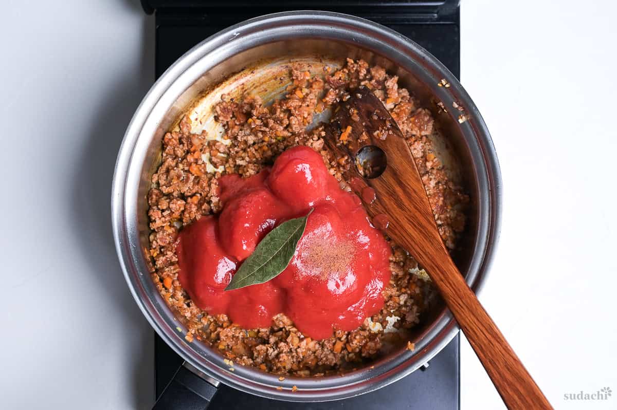 whole canned tomatoes and a bay leaf in spaghetti meat sauce in a pan on the stove top