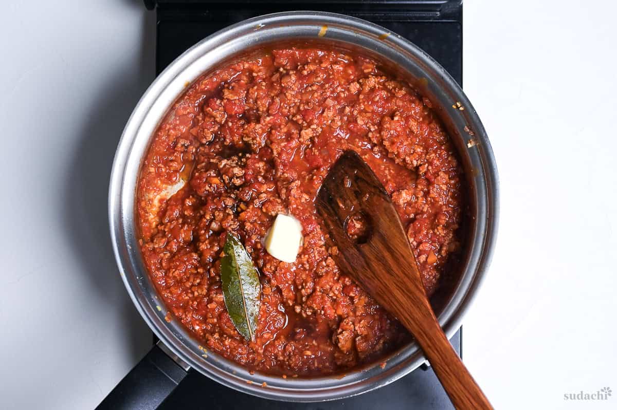 Spaghetti meat sauce simmering in a pan, with a cube of butter melting on top