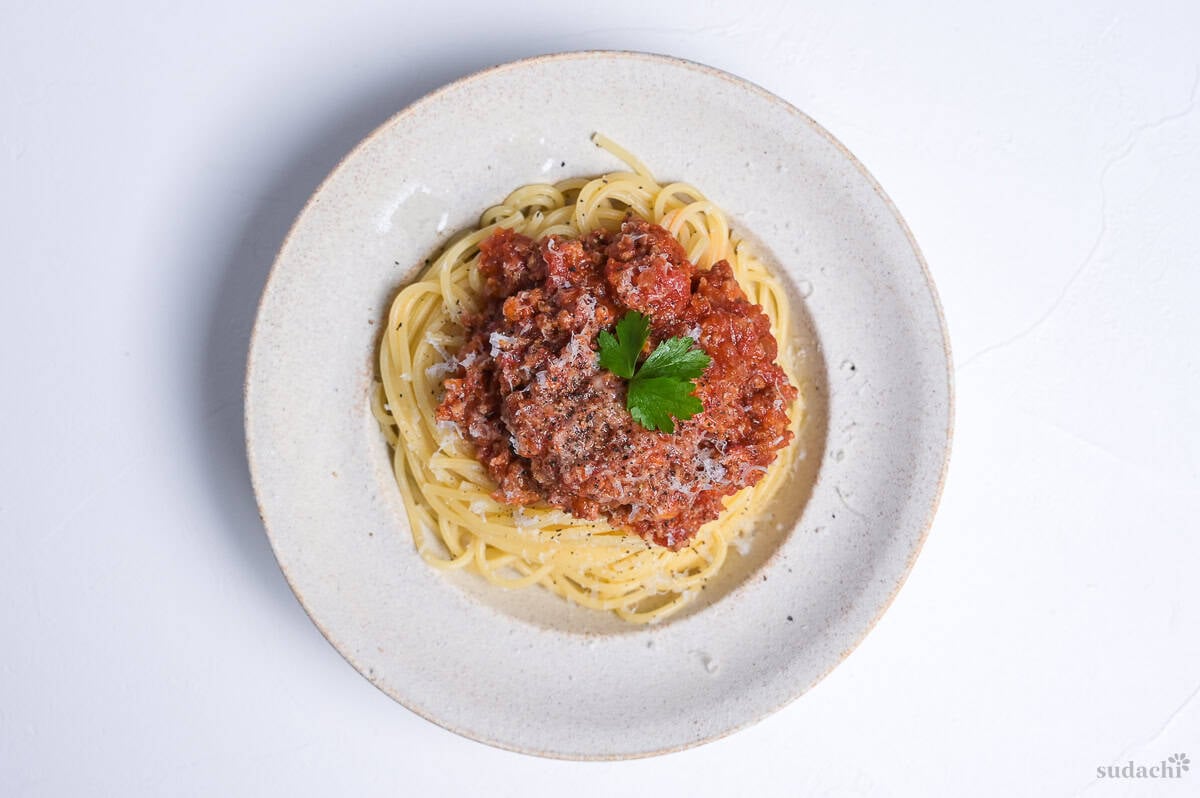 Japanese style spaghetti meat sauce topped with grated cheese and a piece of fresh parsley in an off-white pasta dish