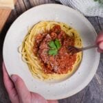 Japanese style spaghetti meat sauce topped with grated cheese and a piece of fresh parsley in an off-white pasta dish with a fork going in thumbnail
