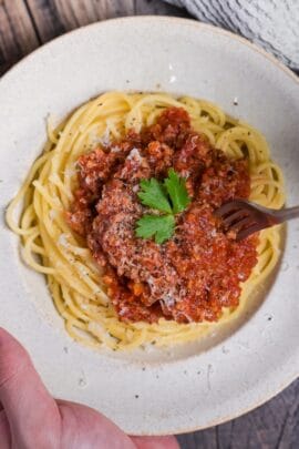 Japanese style spaghetti meat sauce topped with grated cheese and a piece of fresh parsley in an off-white pasta dish with a fork going in thumbnail