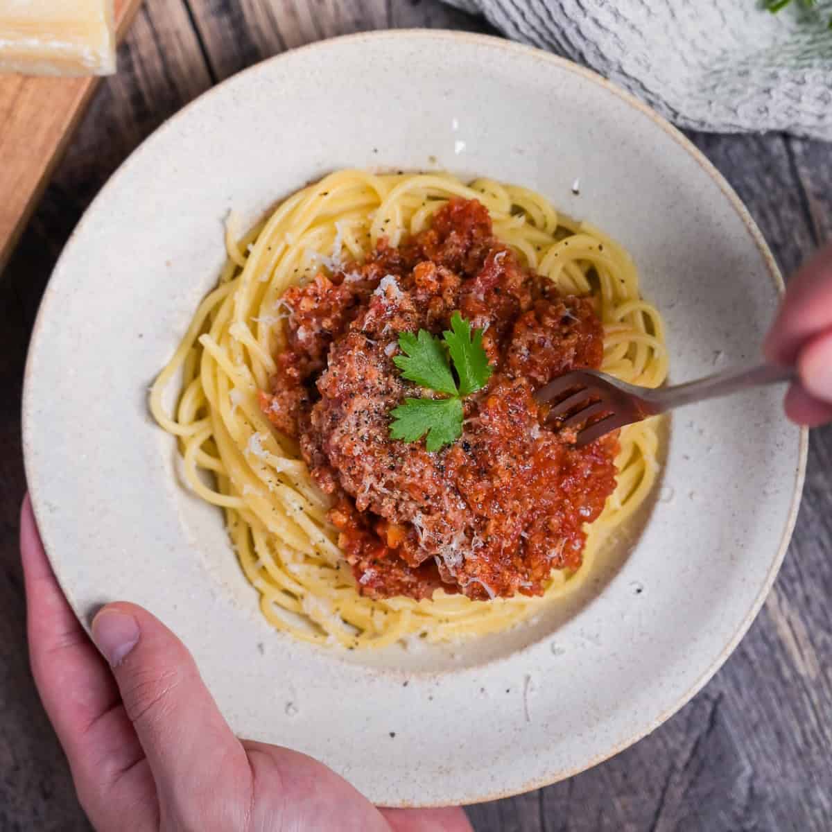 Japanese style spaghetti meat sauce topped with grated cheese and a piece of fresh parsley in an off-white pasta dish with a fork going in thumbnail