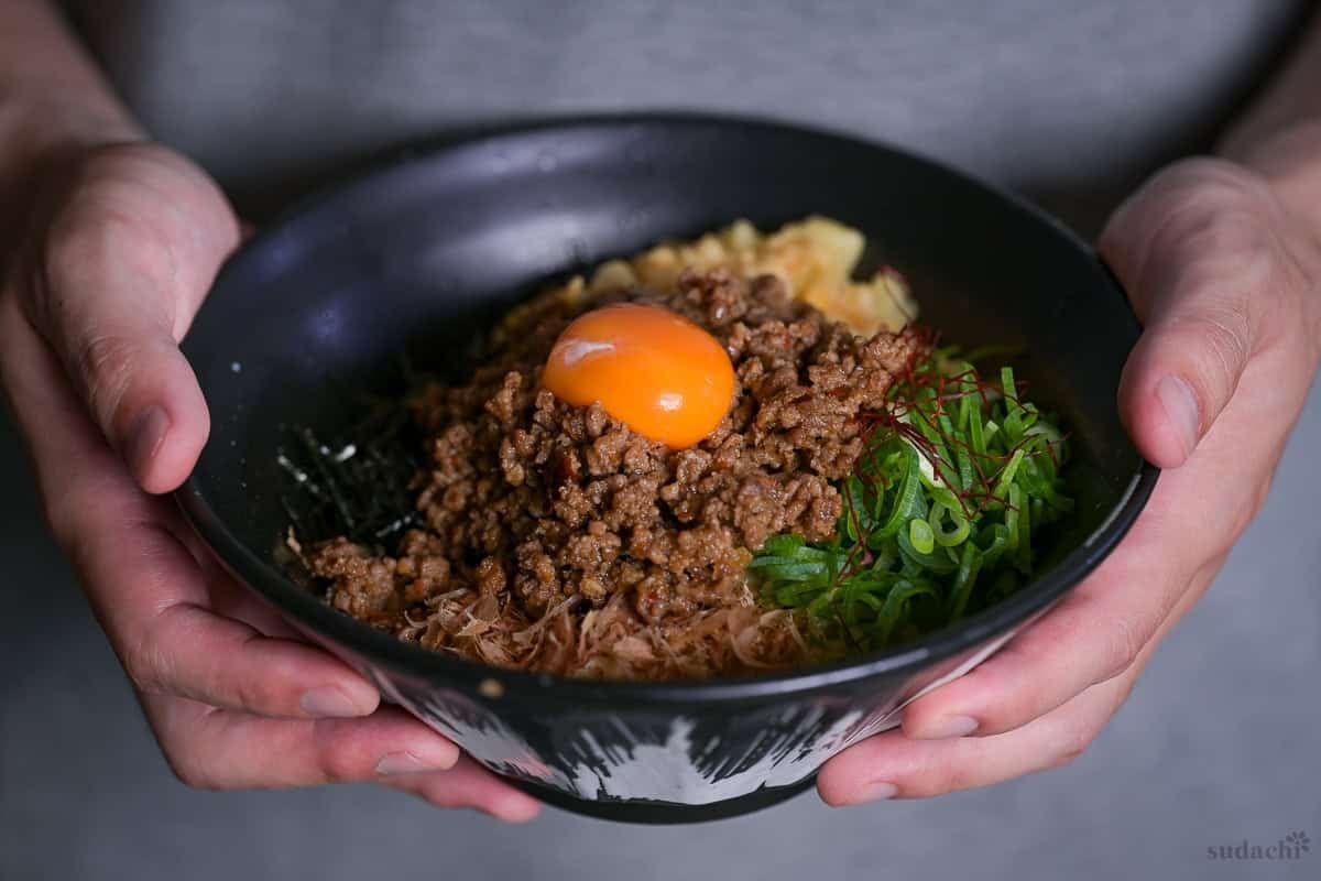 Yuto Omura holding up Taiwan Mazesoba topped with an egg yolk in a black ramen bowl.