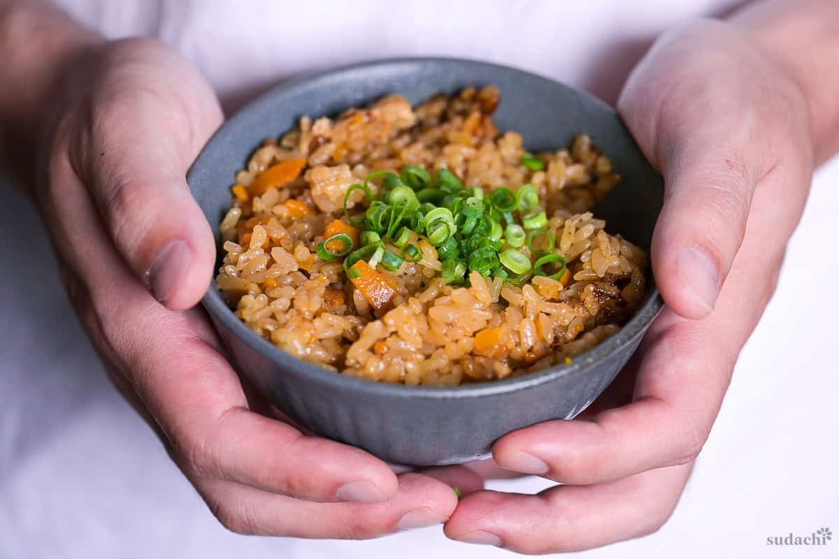Yuto Omura holding up takikomi gohan sprinkled with chopped green onions in a gray-blue ceramic rice bowl