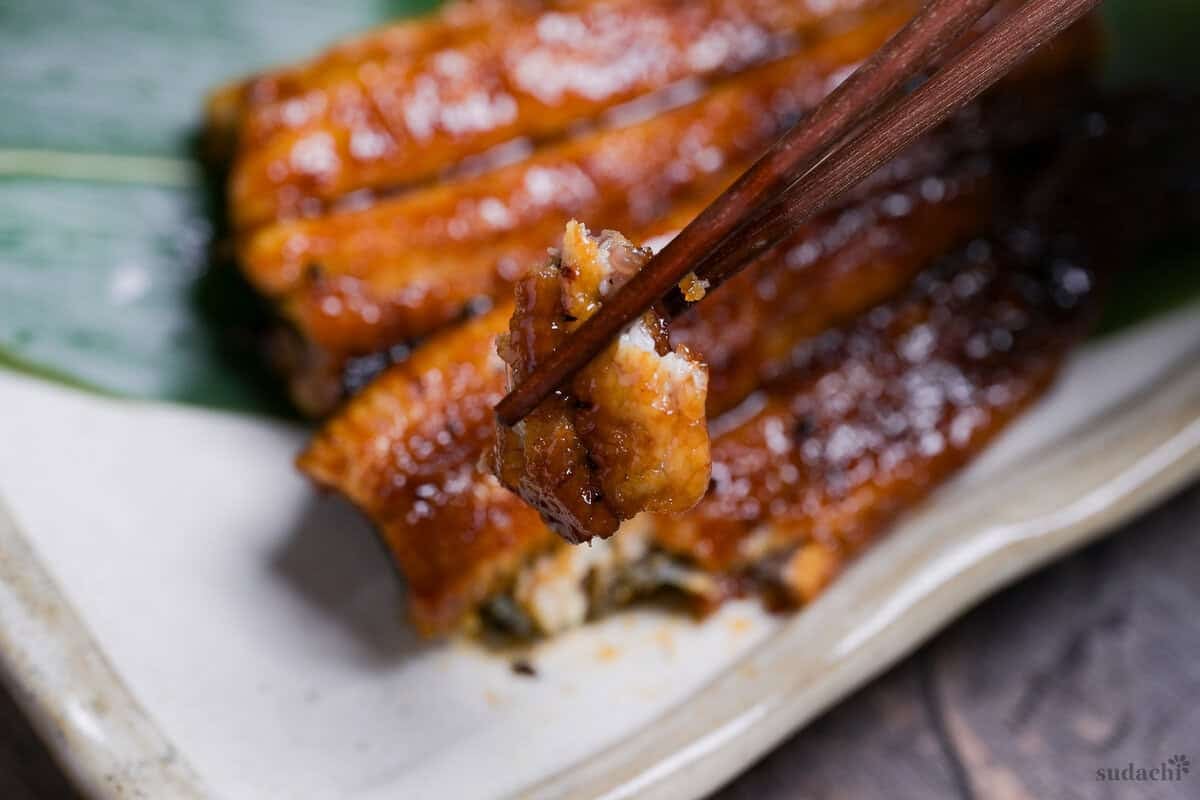 A close up of unagi kabayaki held up with wooden chopsticks