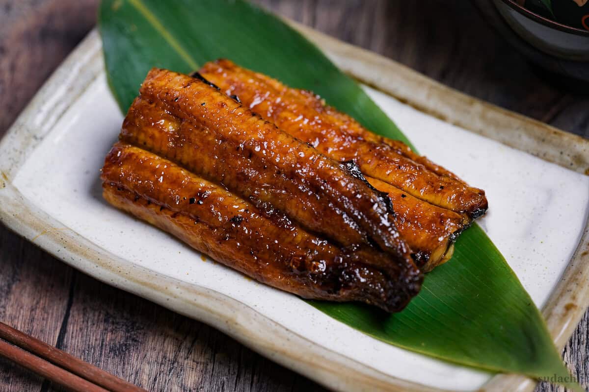 Unagi kabayaki served on a bamboo leaf on a cream rectangular plate with light brown rim