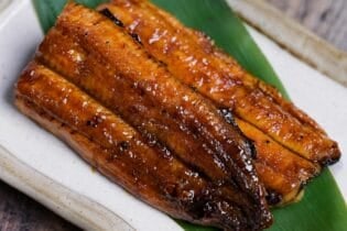 Unagi kabayaki served on a bamboo leaf on a cream rectangular plate with light brown rim