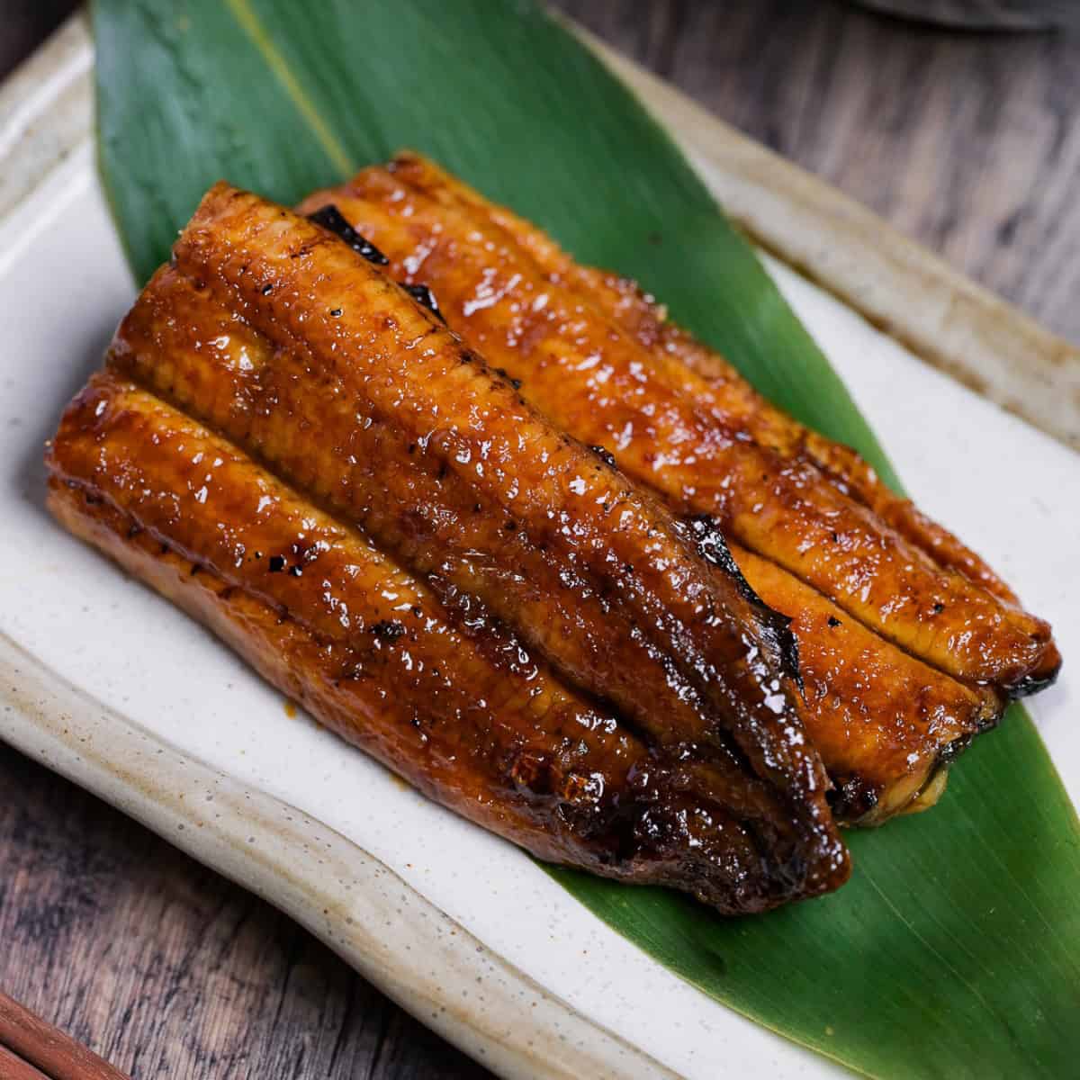 Unagi kabayaki served on a bamboo leaf on a cream rectangular plate with light brown rim