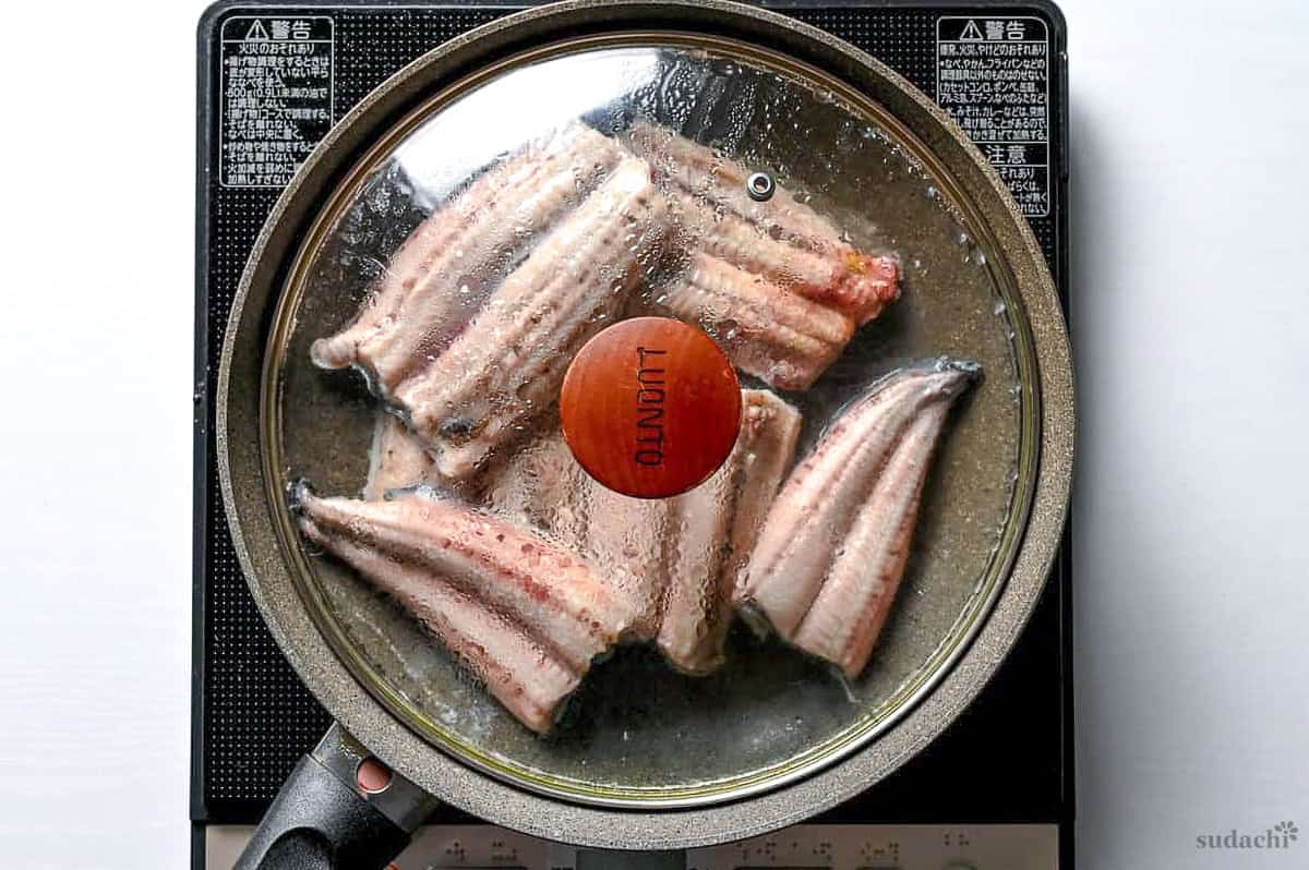 unagi steaming in a frying pan with a clear lid on the stove top