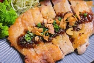 Japanese style pan fried chicken steak with homemade sauce and crispy garlic chips on a blue plate