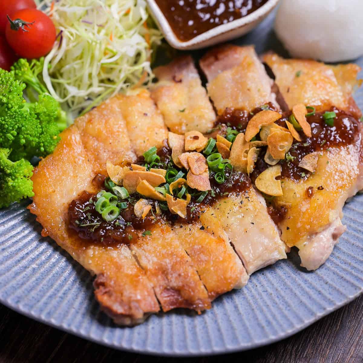 Japanese style pan fried chicken steak with homemade sauce and crispy garlic chips on a blue plate