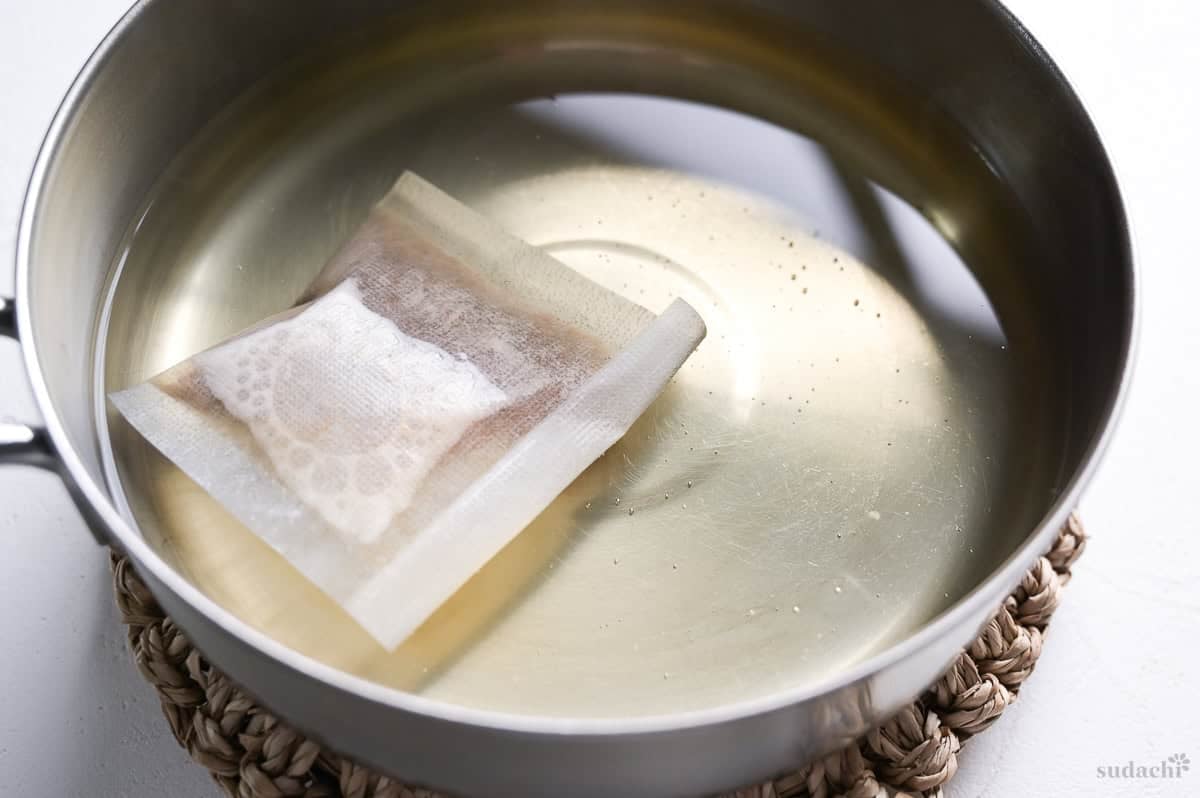 Dashi packet simmered in soft water in a saucepan on a Japanese style woven trivet.
