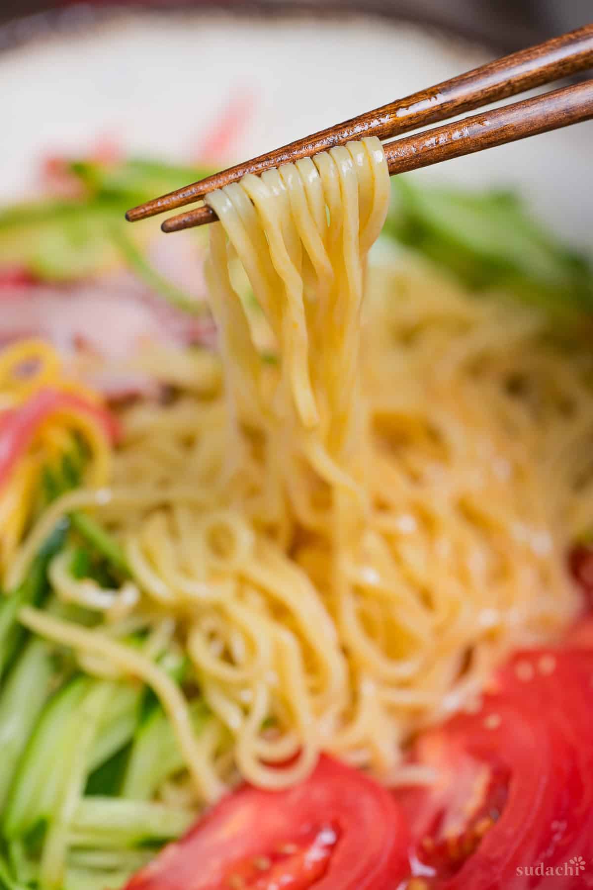 Close up of noodles from hiyashi chuka held up with wooden chopsticks.