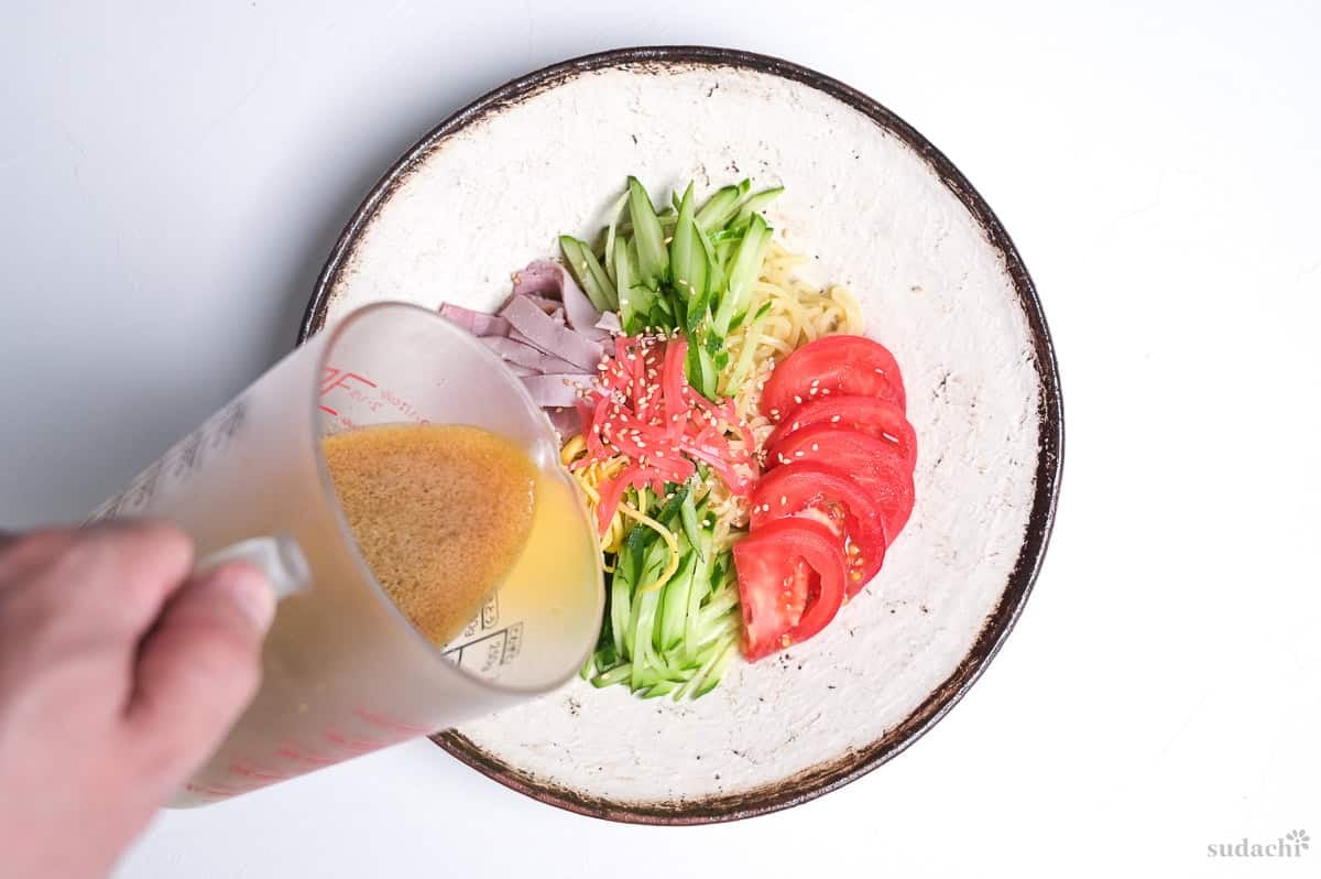 Pouring sauce over hiyashi chuka on a cream-colored plate with brown rim.