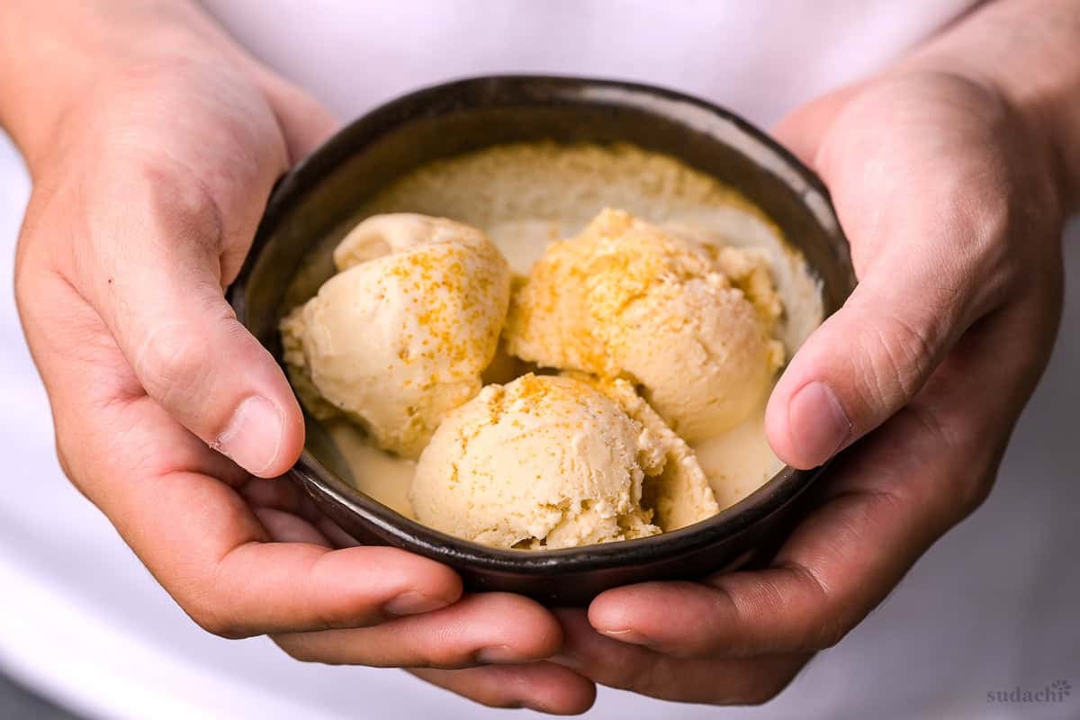 Yuto Omura holding up a bowl with three scoops of hojicha ice cream sprinkled with hojicha tea powder